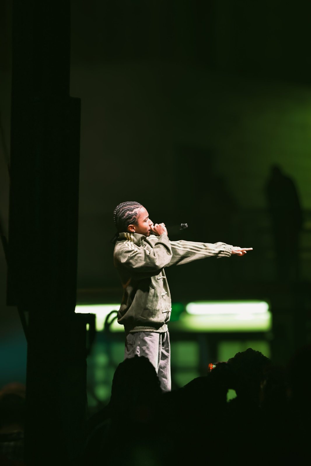 Performer in a track jacket pointing at the crowd under green light